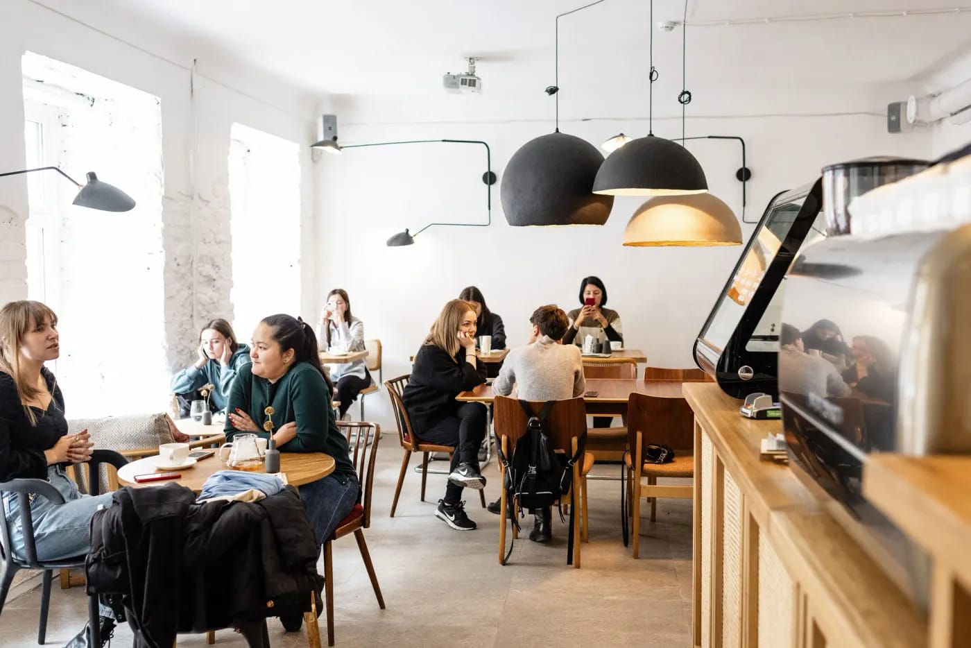 Young people chatting at tables in a bright, independent café with an espresso machine on the counter