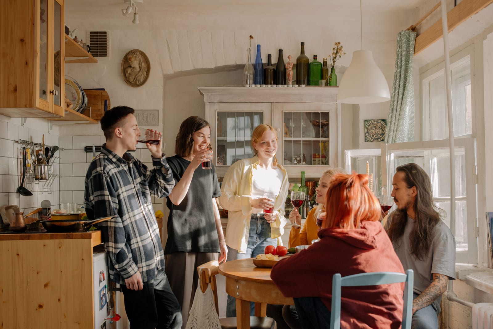 A group of students chatting and sharing drinks around the table in a cosy shared kitchen