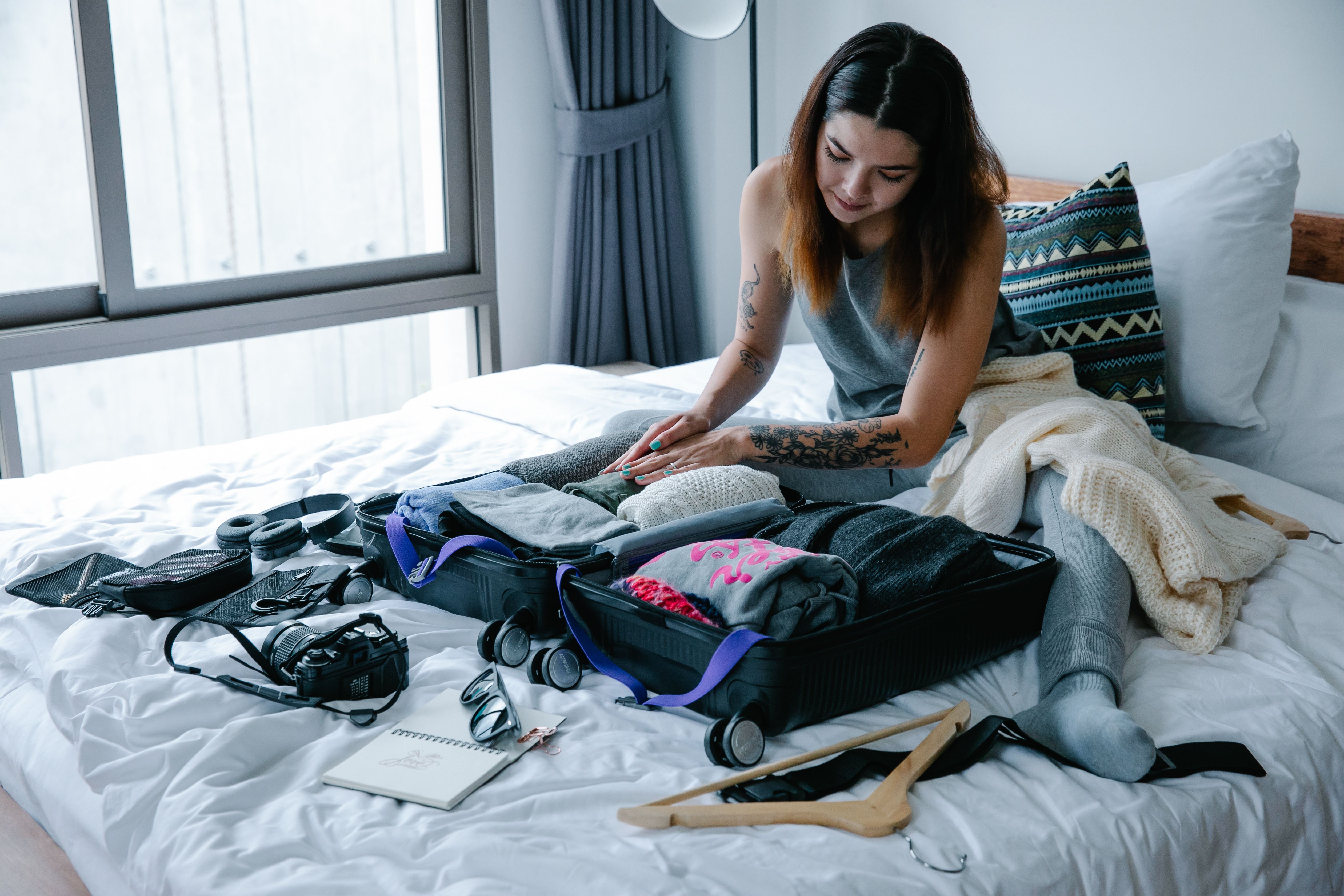 A flat-lay of student travel kit: backpack, water bottle, passport, boarding pass, camera, packing cubes, sunglasses and a book
